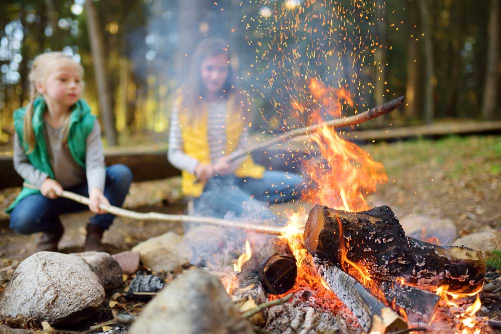 two girls with sticks beside campfire