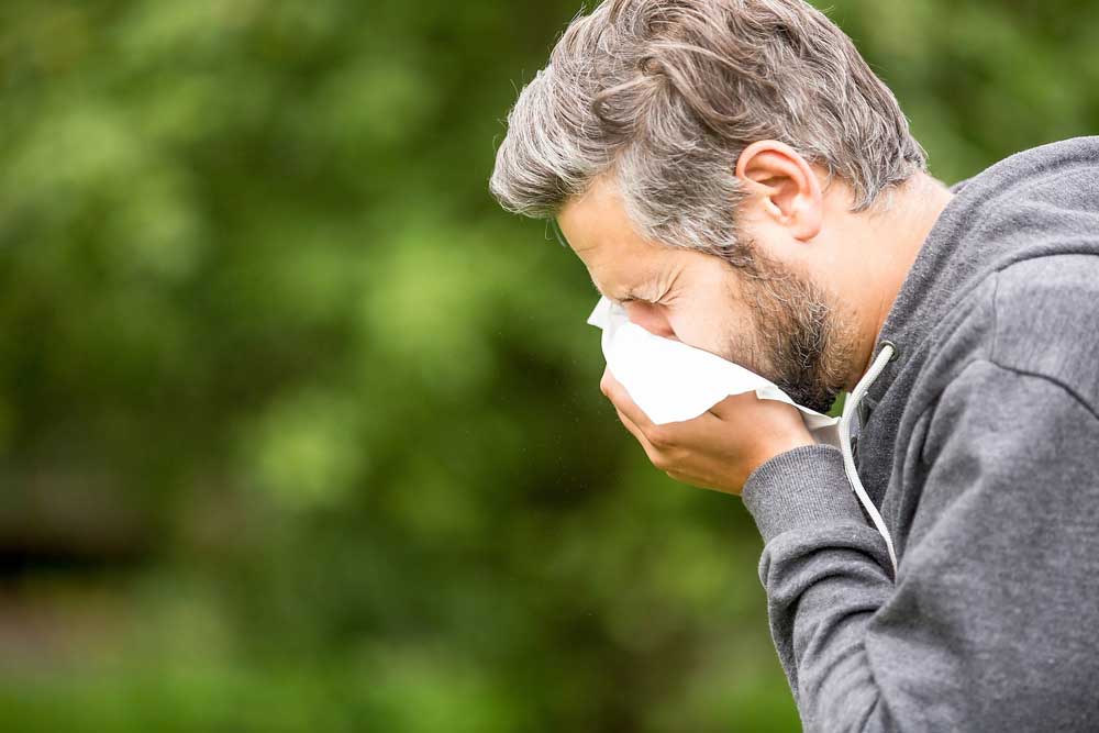 man sneezing into tissue outside