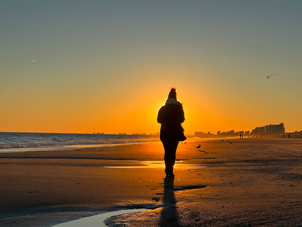silhouette of person walking into sunset on beach 