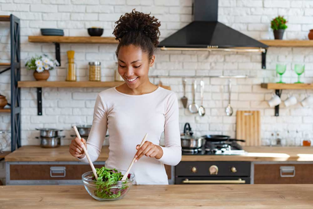 Young woman mixes salad in glass bowl in bright kitchen