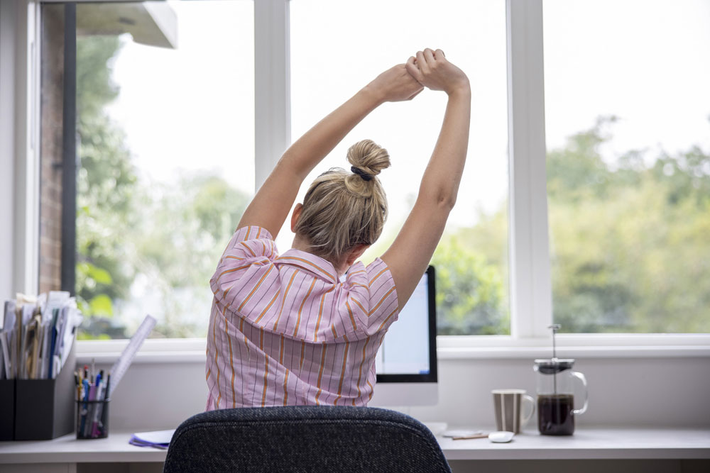 woman from behind sitting at desk stretching arms overhead