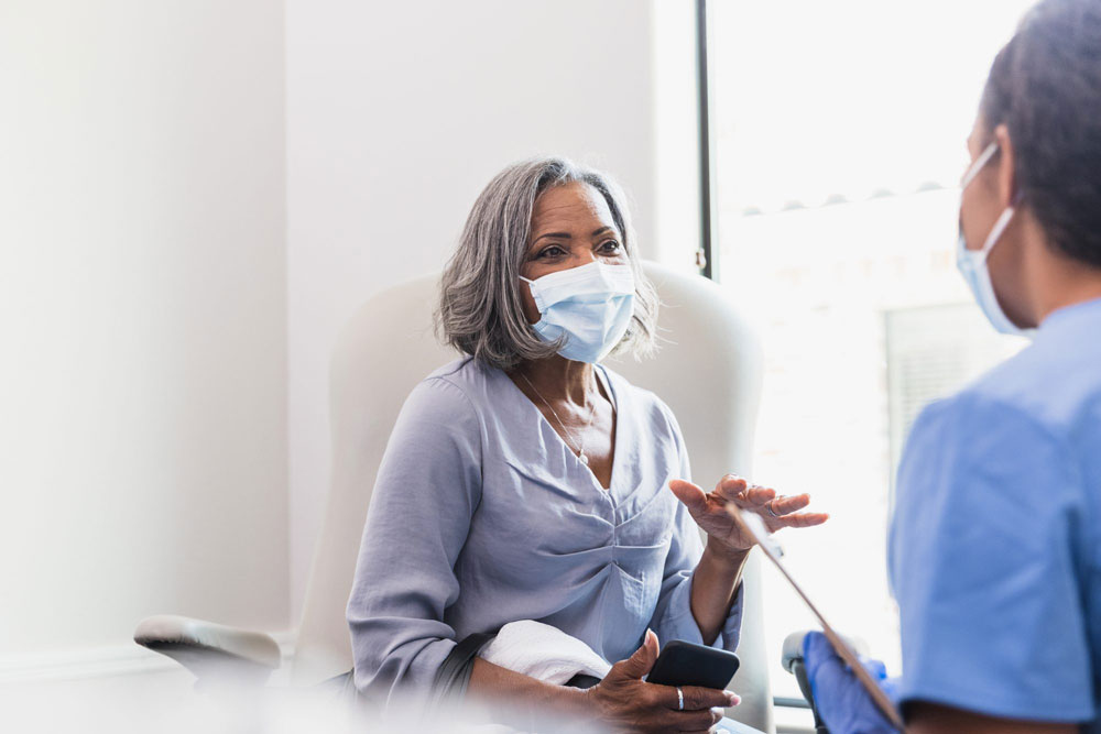 older woman wearing mask talking with doctor in exam room
