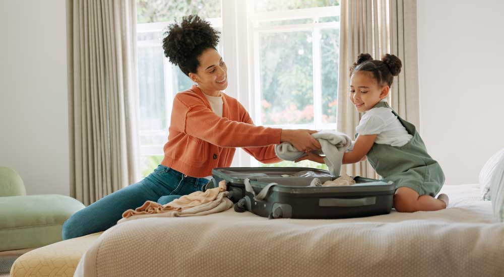 mother packing suitcase on bed with little girl