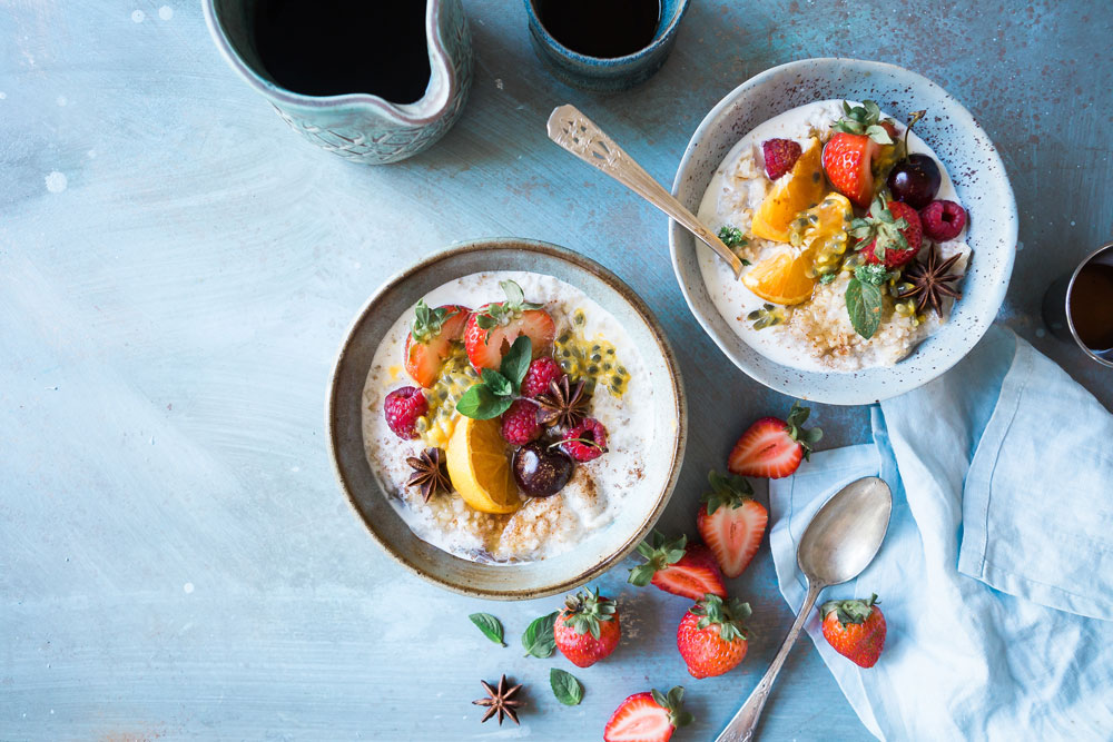 two bowls of oatmeal topped with fresh fruit on blue table