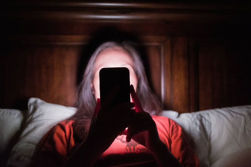 woman looking at brightly lit cell phone in dark room