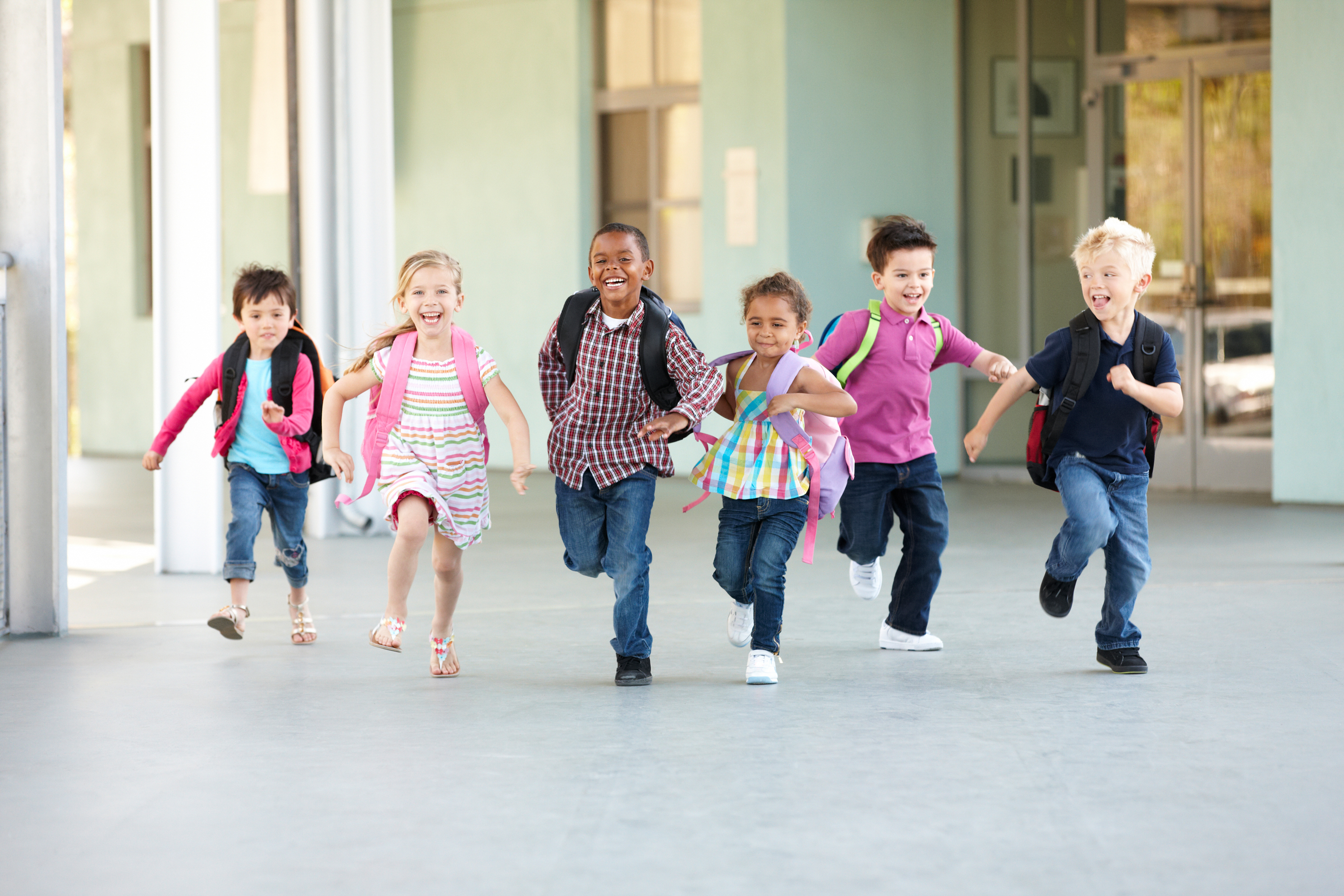 A group of children of different genders and ethnicities runs down a hallway.