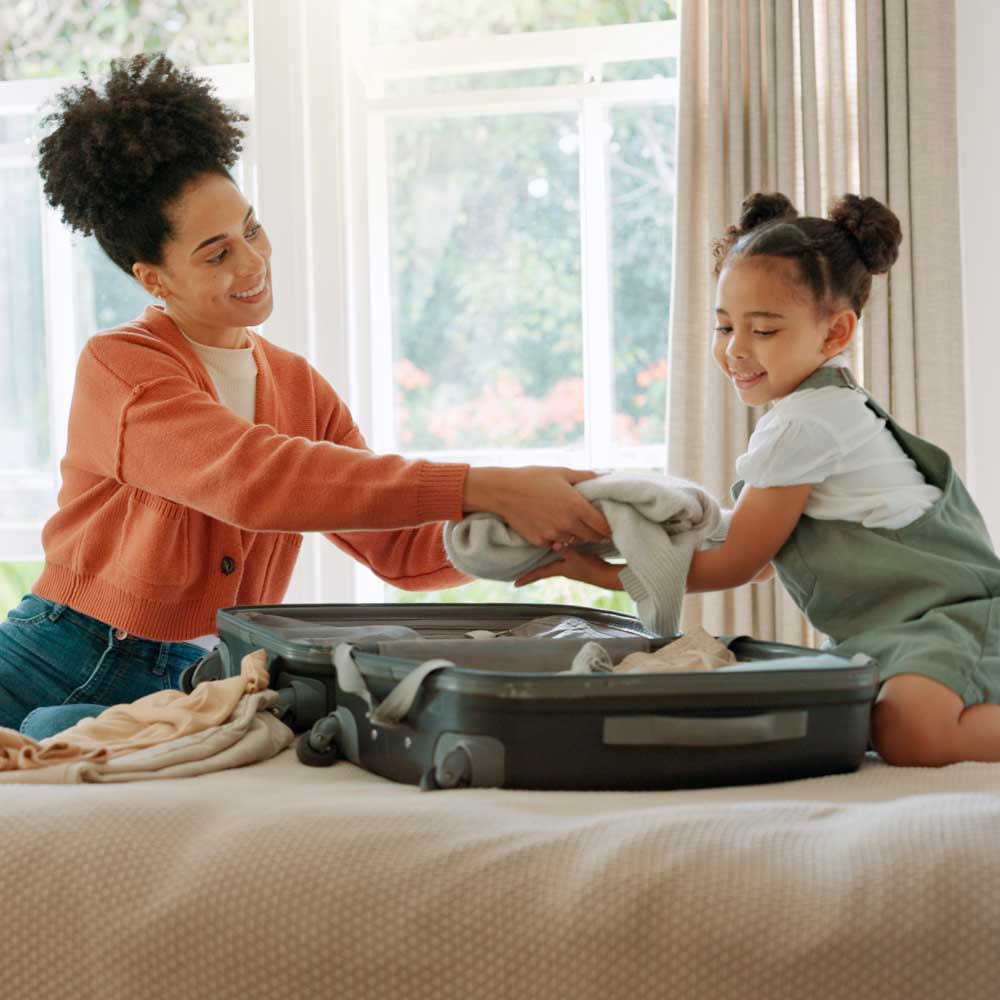 woman sitting on bed with little girl and suitcase
