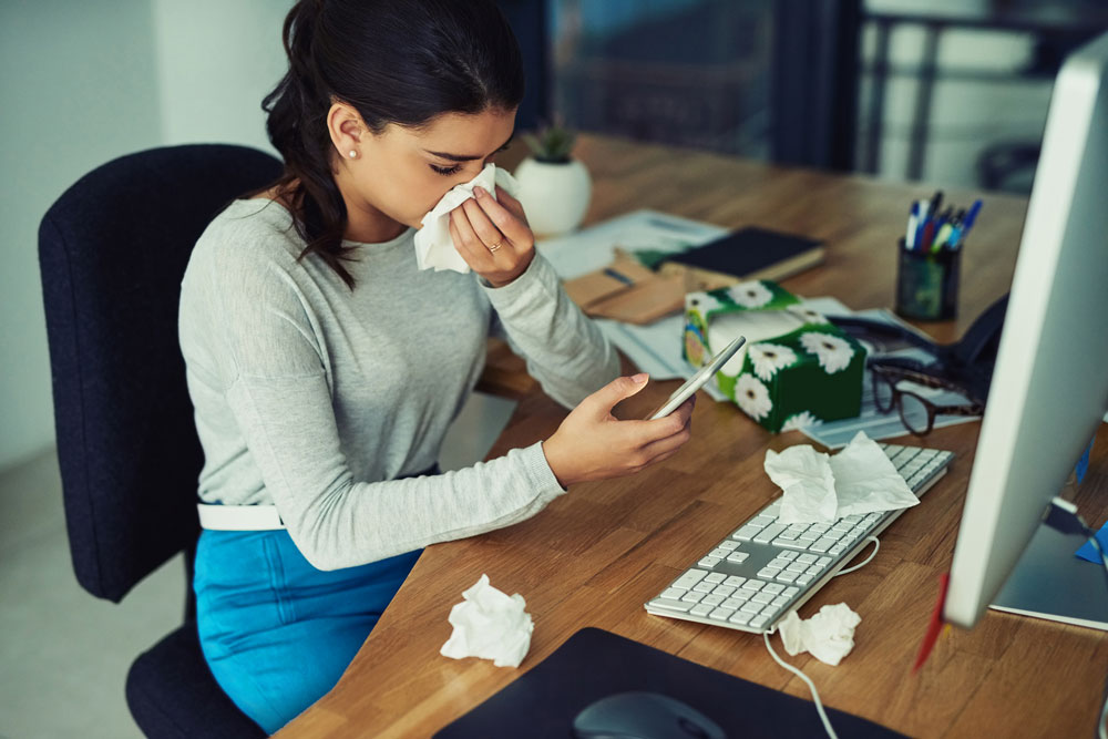 woman sits at desk with tissues and cell phone