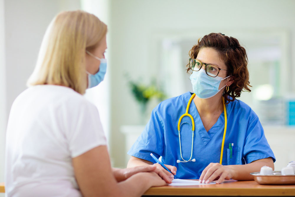doctor in blue scrubs wearing mask talks to patient in mask