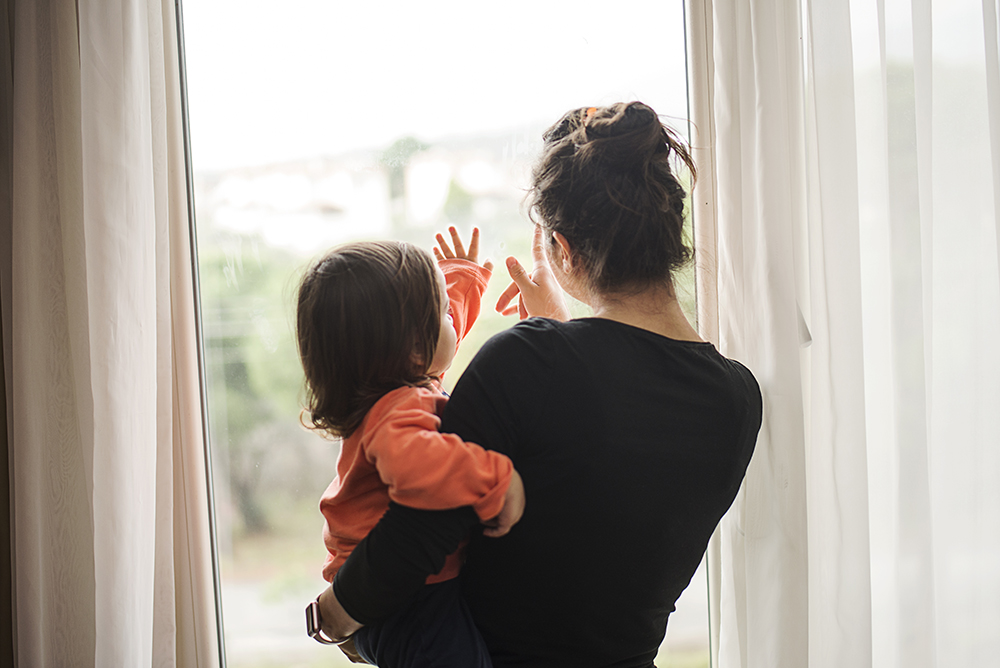 Young woman with toddler daughter looking out window