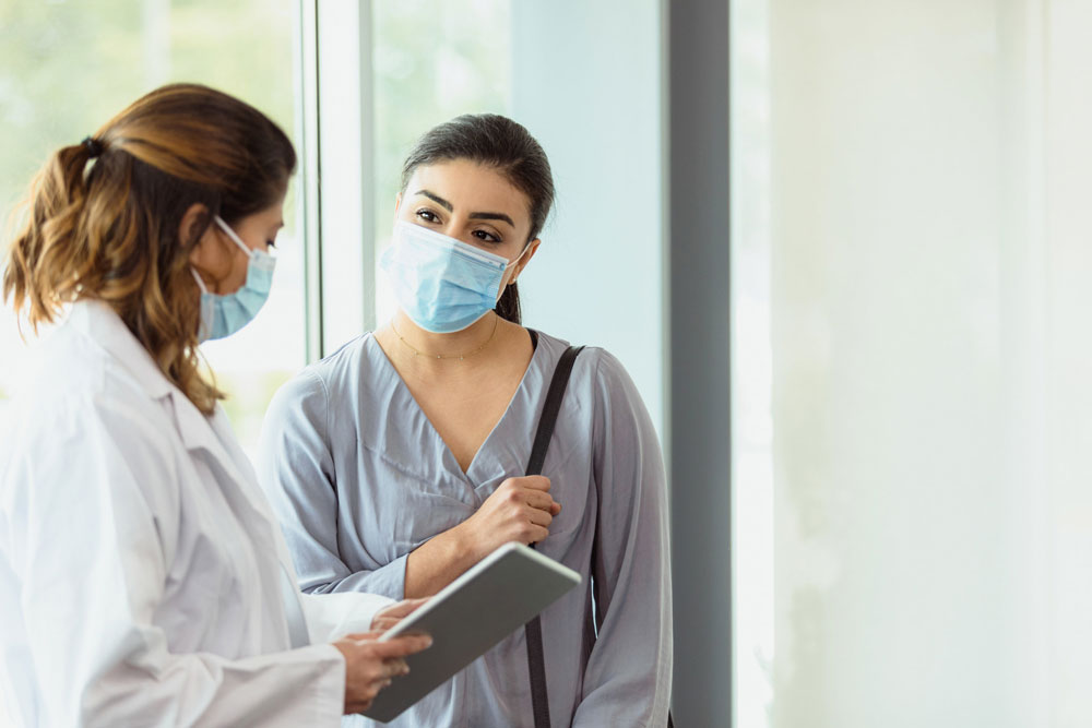 patient wearing mask talks with doctor in hallway