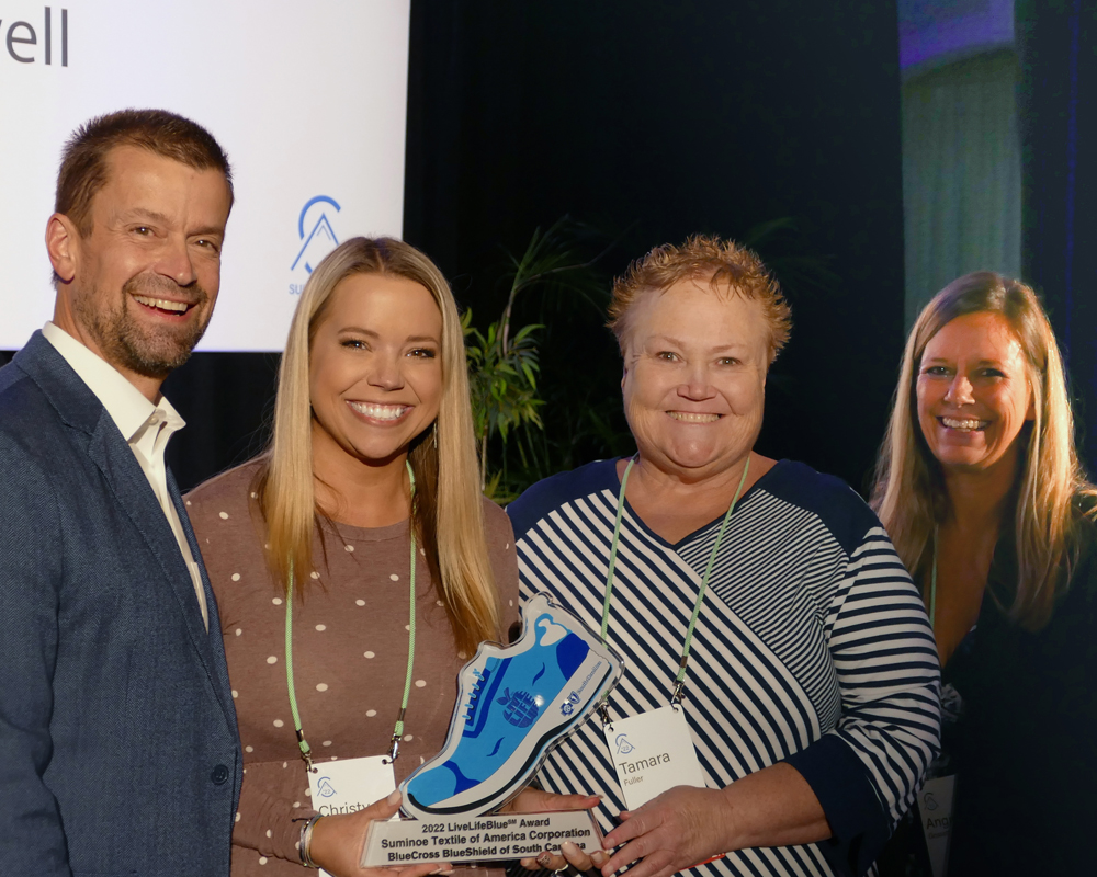 Three women hold blue shoe award next to man in suit