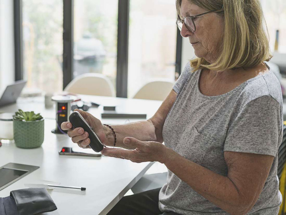 A woman sits at a table and uses a glucose meter to check her blood sugar.