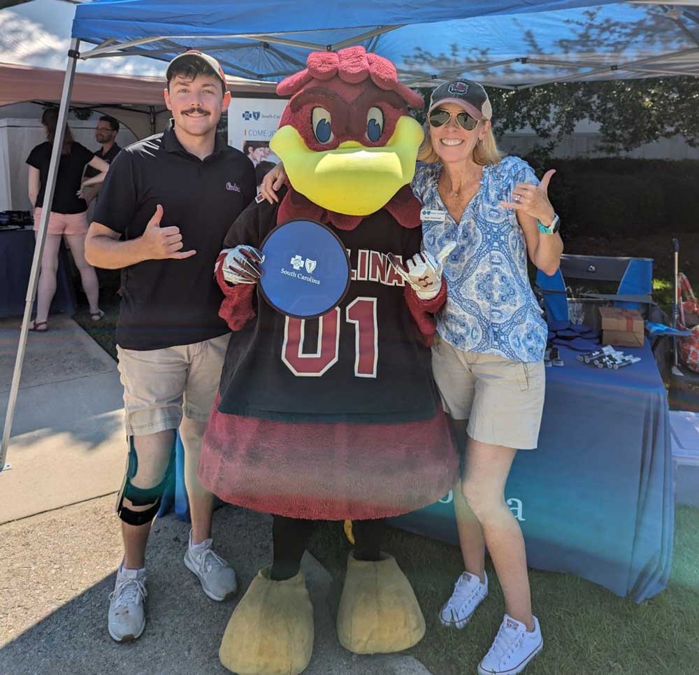 man and woman posing with cocky mascot holding blue cross sign