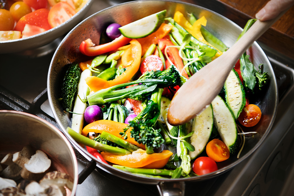 A pan filled with colorful vegetables sizzling on a stove, showcasing a vibrant cooking scene.