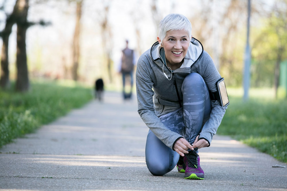 older woman ties shoes on path outside