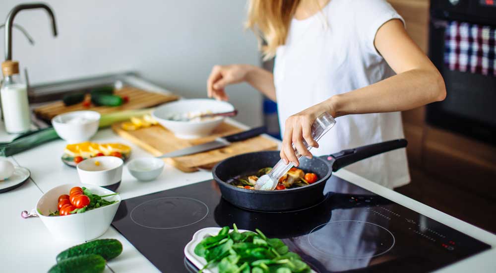 person standing at stove with fresh vegetables 
