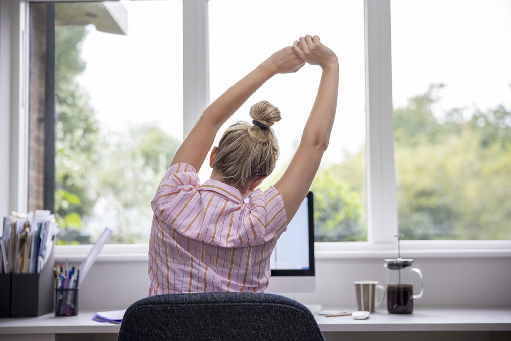 back of woman sitting at desk stretching arms overhead