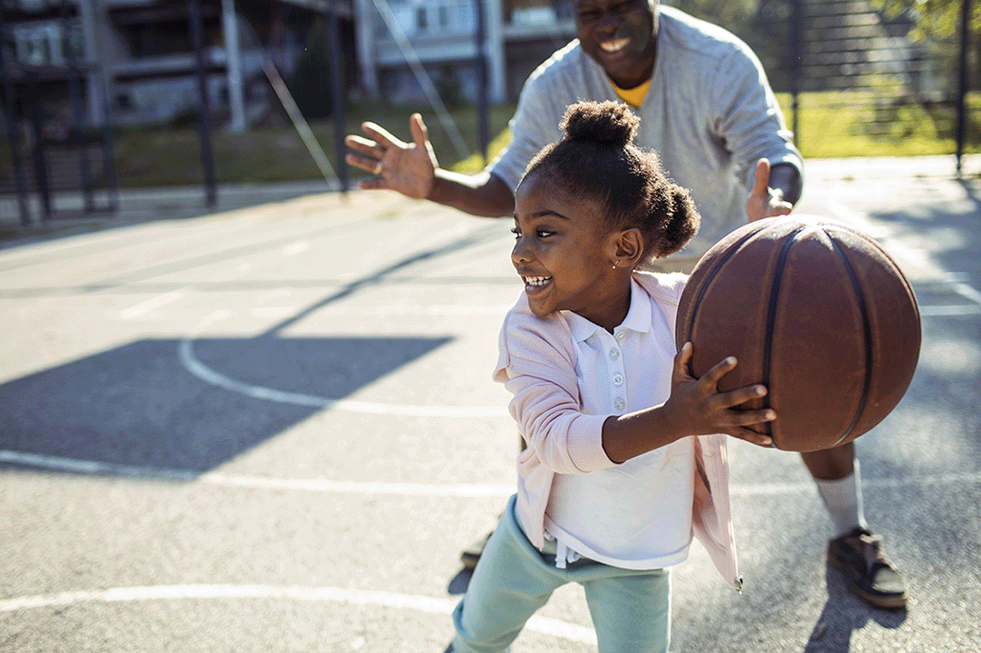 A young girl plays basketball with her father.