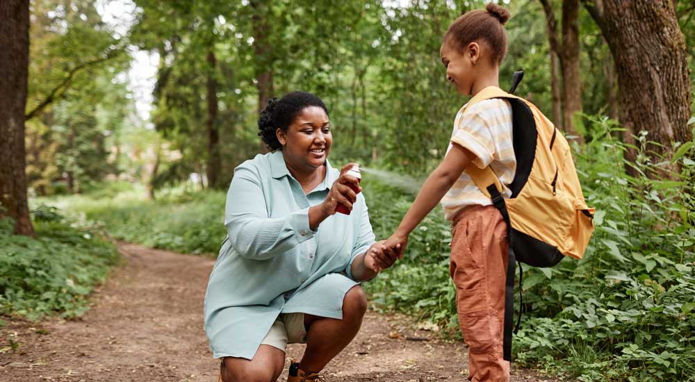 mother applying bug spray to child's arm in nature