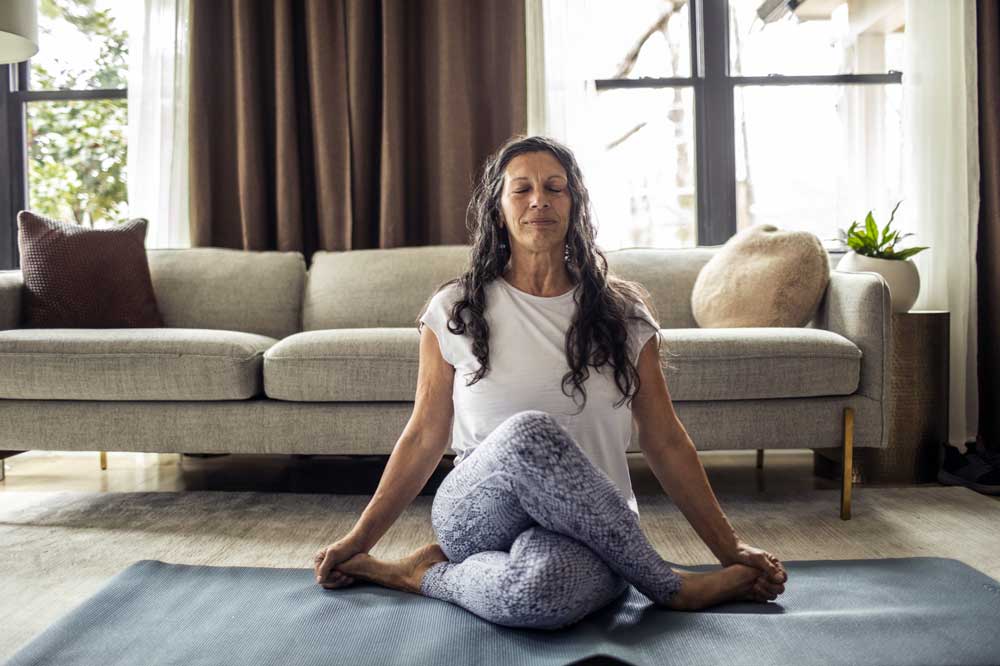 woman sits cross-legged on yoga mat on floor