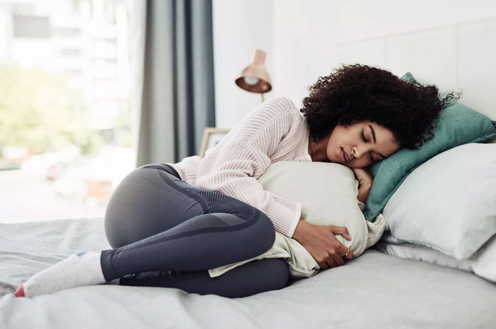 woman curled up in bed holding pillow with sad expression