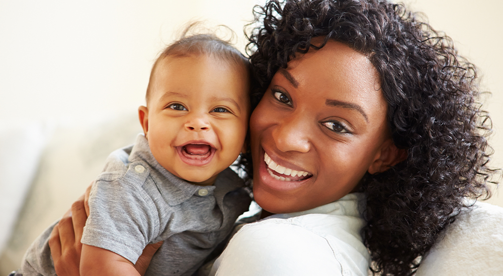 A joyful woman smiles while gently cradling a baby in her arms, radiating warmth and love.