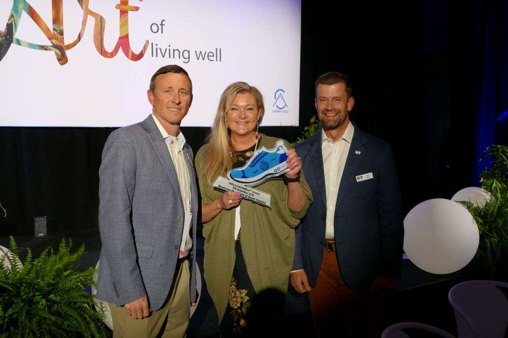 three people smiling and one holds blue shoe award