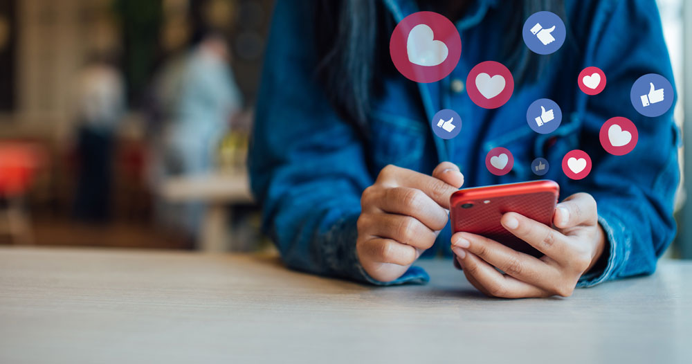 person holding phone with likes and heart illustrations floating from phone