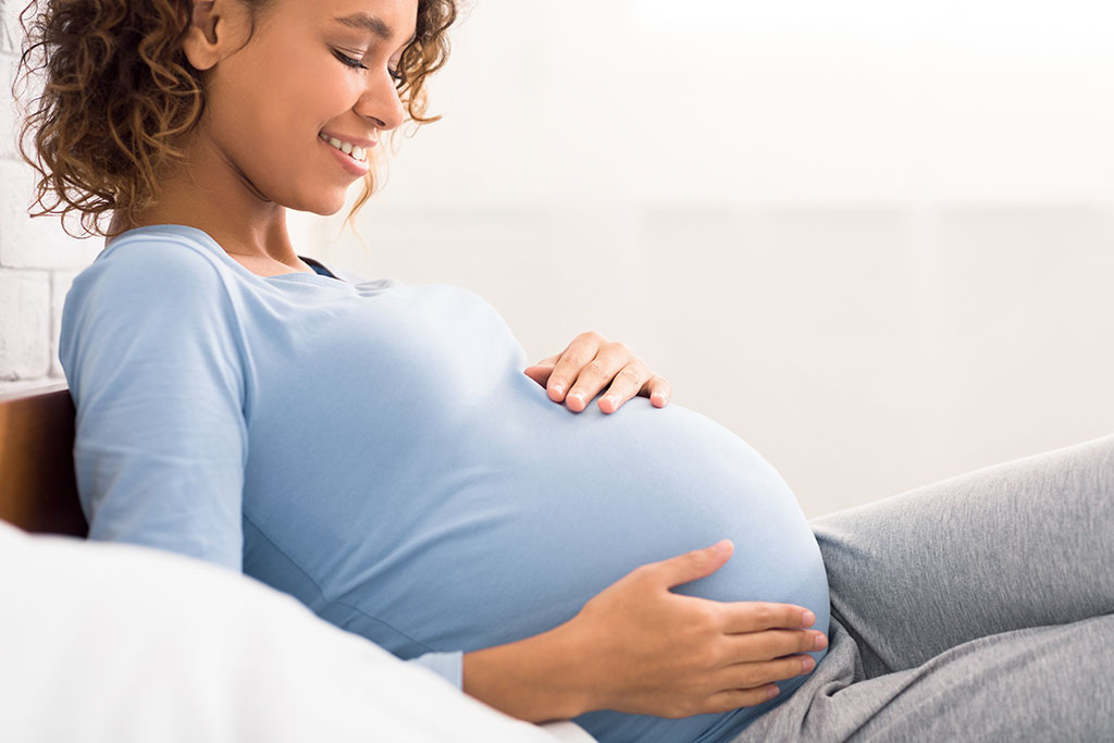 A pregnant woman smiles and looks down as she cradles her belly
