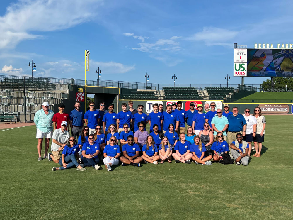 group of interns on baseball field in blue shirts