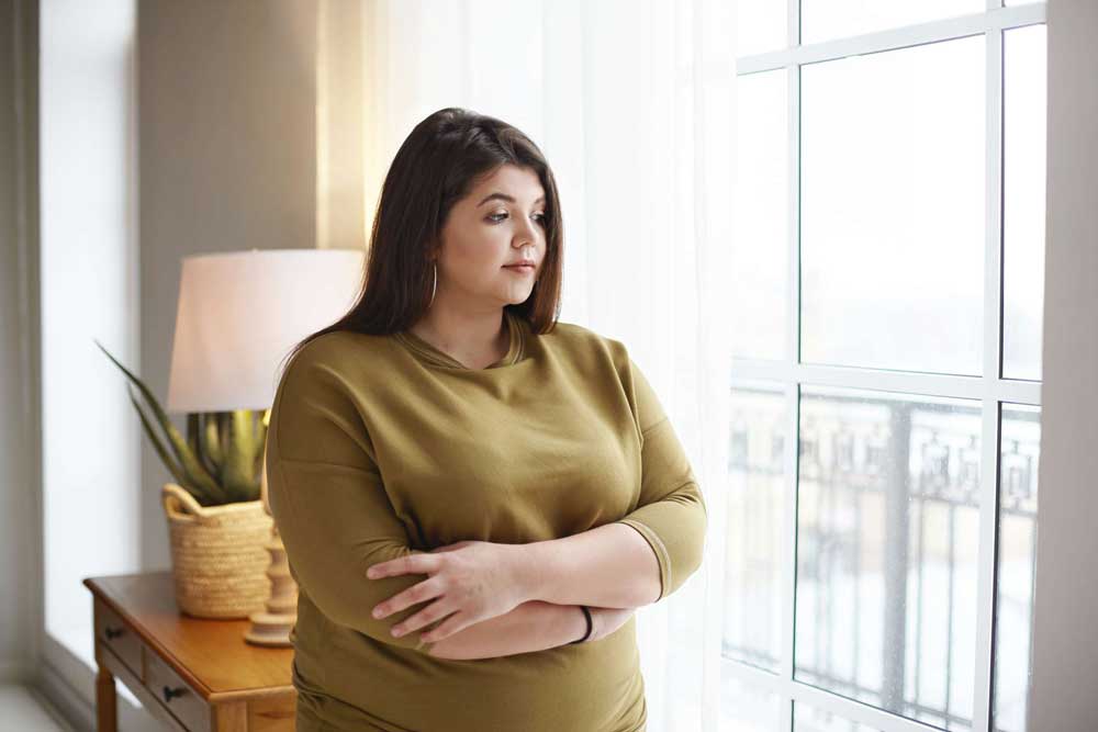 young girl holds arms around stomach and looks out window