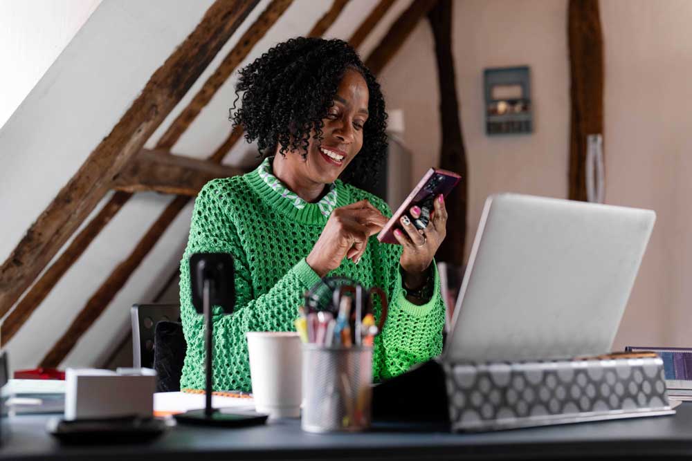 woman at computer looking at phone