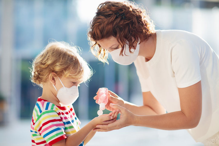 woman helps kid with hand sanitzier and mask