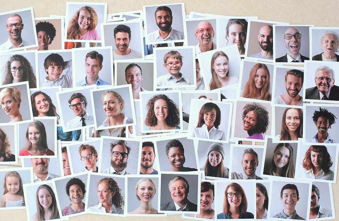 Multiple headshots of people of different age, gender and ethnicity are spread out across a surface.
