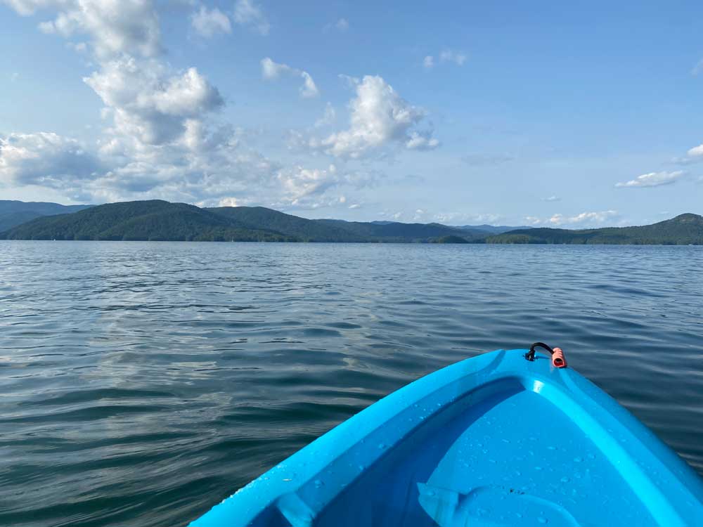 front of kayak on water with mountains and blue sky