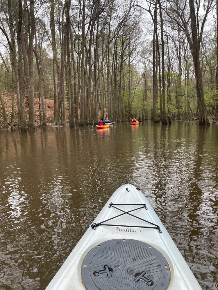 Front of kayak on river with other kayakers in the distance