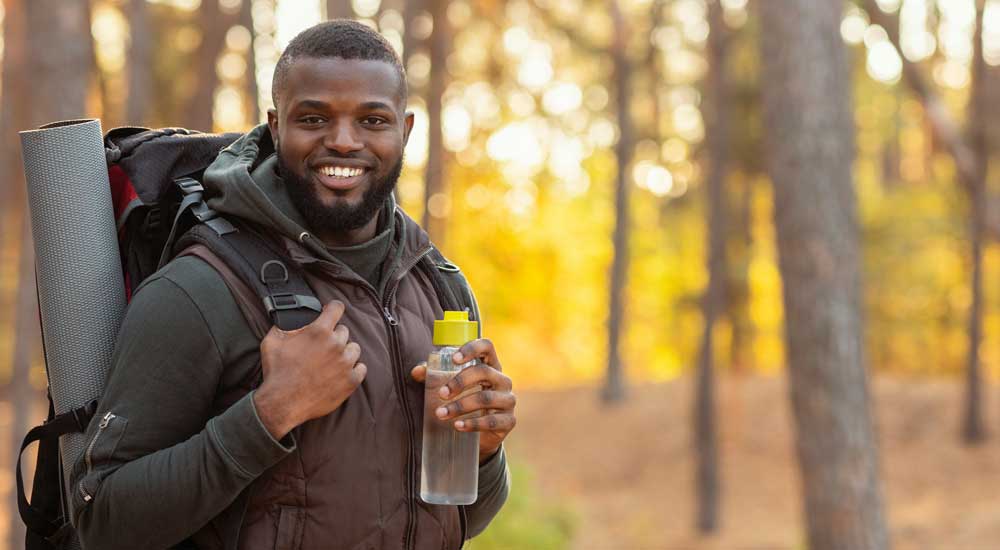 Man wearing backpack in woods holding water bottle