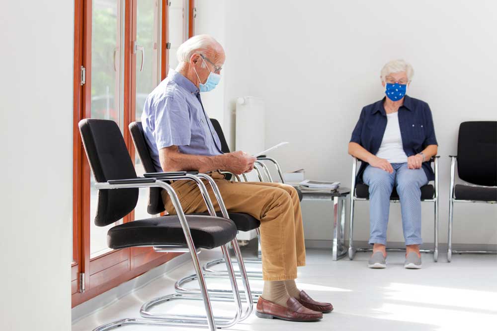 elderly man sits in waiting room wearing a mask