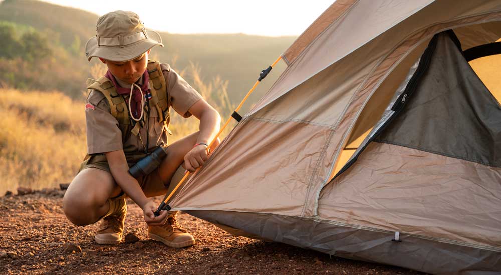 young boy in uniform putting tent into ground outside