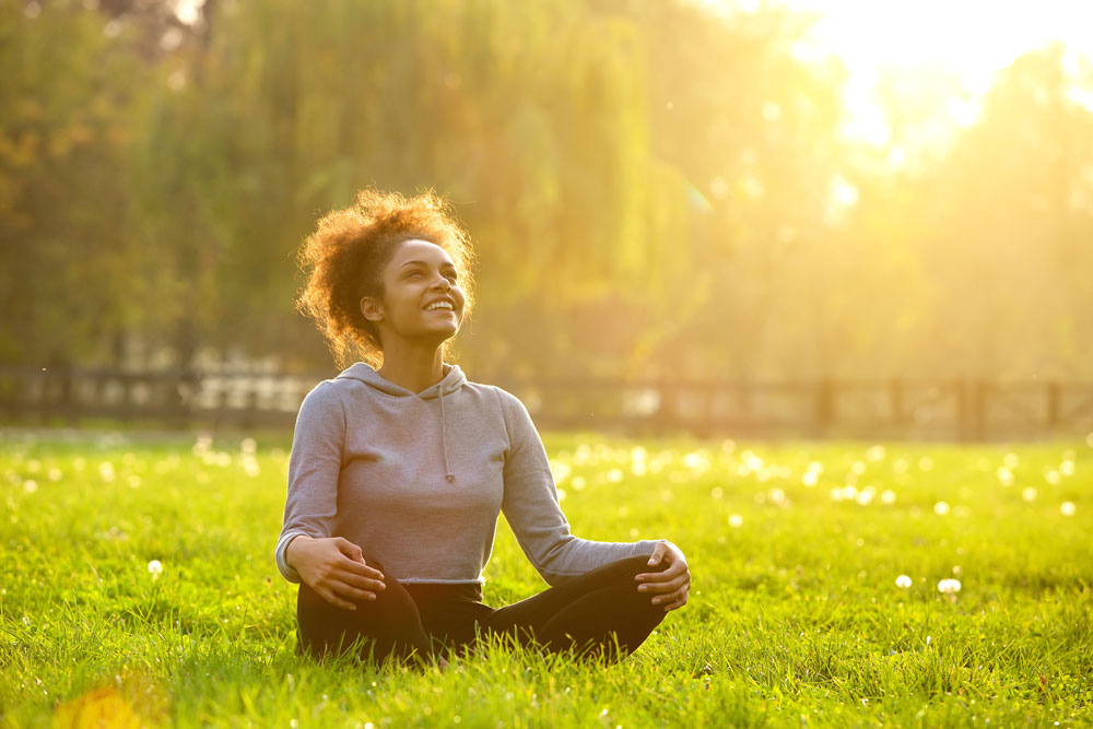 woman sits crosslegged in field with sunshine