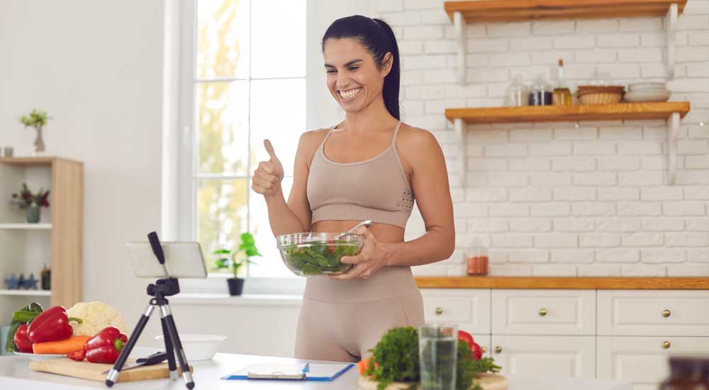 woman in kitchen with salad bowl filming on phone