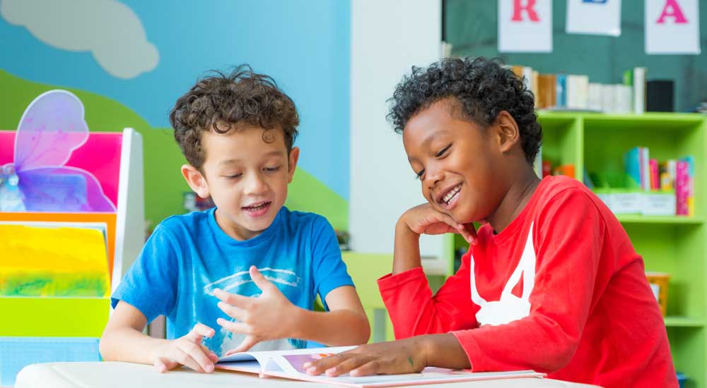 two children in bright classroom reading book