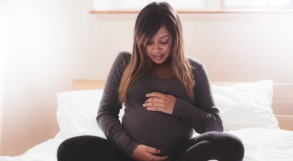 woman sitting on bed holding pregnant belly