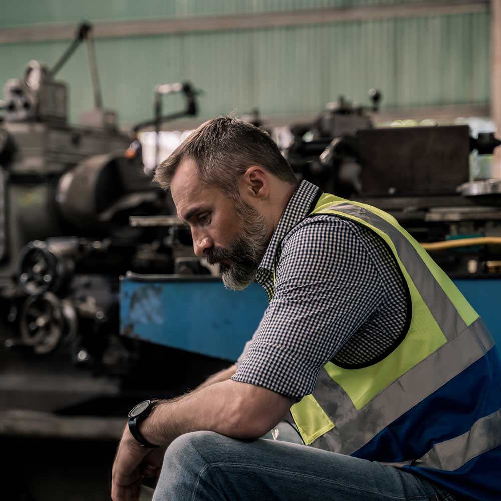 man in work vest at manufacturing warehouse looking sad