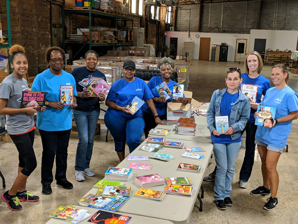 group of employees in blue shirts holding books around table