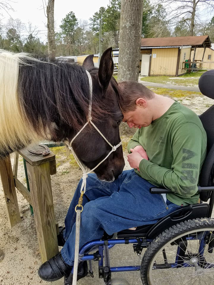man in wheelchair with head against a horse's head