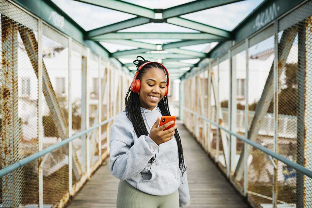 young woman outside holding phone wearing headphones