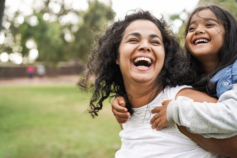 woman holding little girl on back outside smiling 