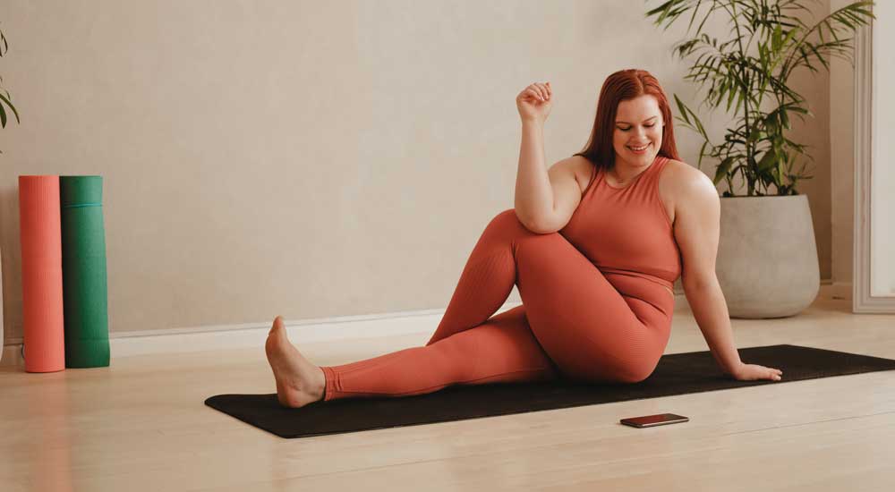 woman doing yoga on mat with phone 